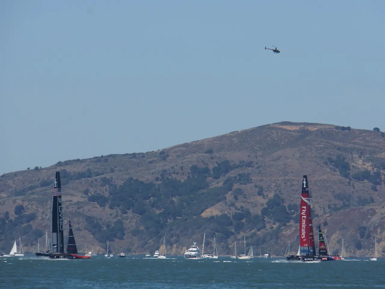 In the image I can see a beach in which there are some boats, ships and also I can see a mountain,...