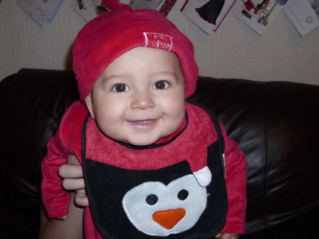 In the picture we can see a baby, child sitting on a sofa which is brown in color and child with...