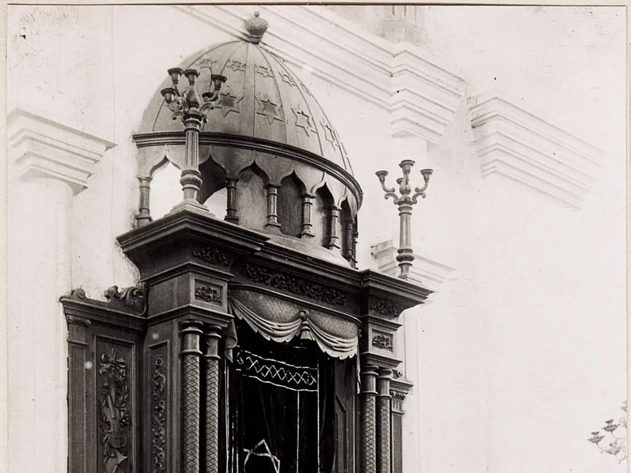 The image shows an old black and white photo of a building with stairs, railings, pillars, a door,...