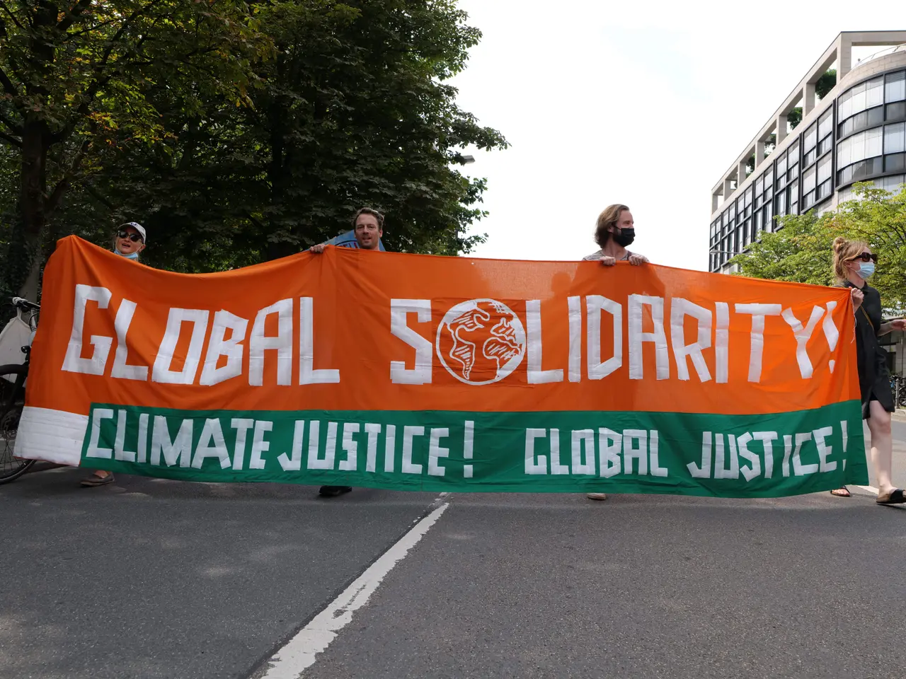 The image shows a group of people walking down a street, holding a banner that reads "Global...
