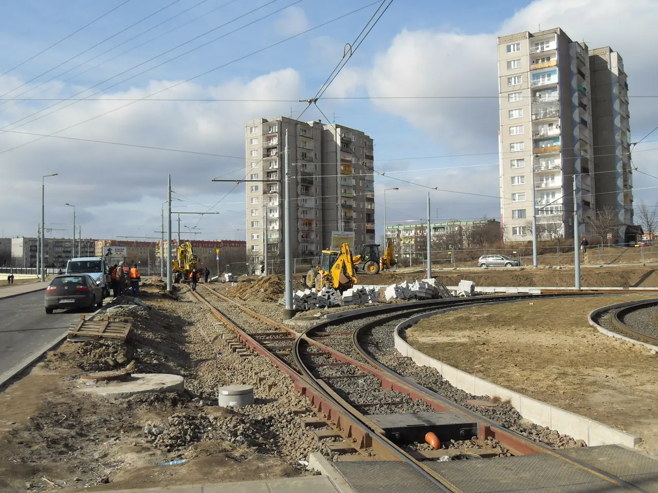 The image shows a construction site with a train track running through it, surrounded by buildings,...