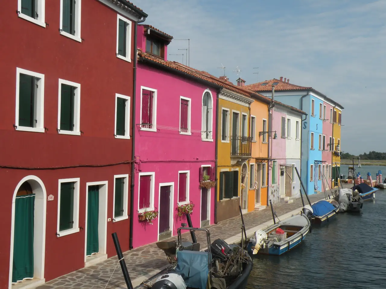 The image shows a picturesque scene of colorful houses in Burano, Venice, Italy, with boats docked...
