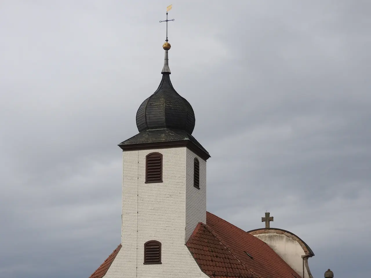 The image shows a church with a steeple and a clock tower in the middle of a street, surrounded by...