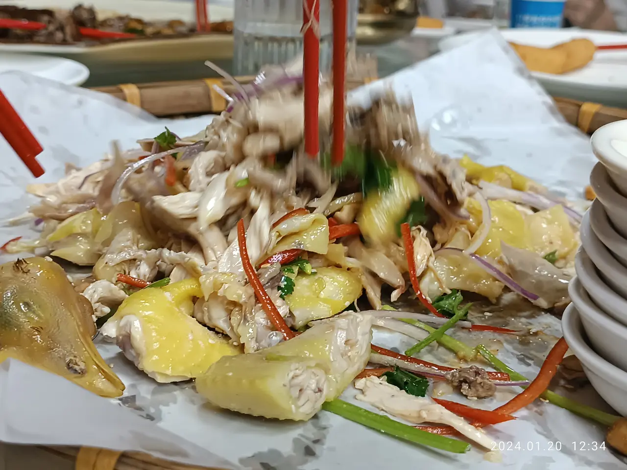 The image shows a table topped with plates of food and bowls of sauce, as well as chopsticks,...