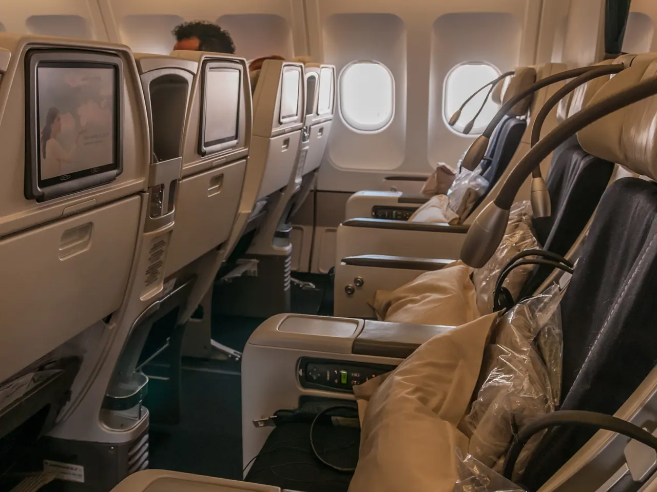 The image shows a row of empty business class seats in an airplane, with a person sitting in one of...