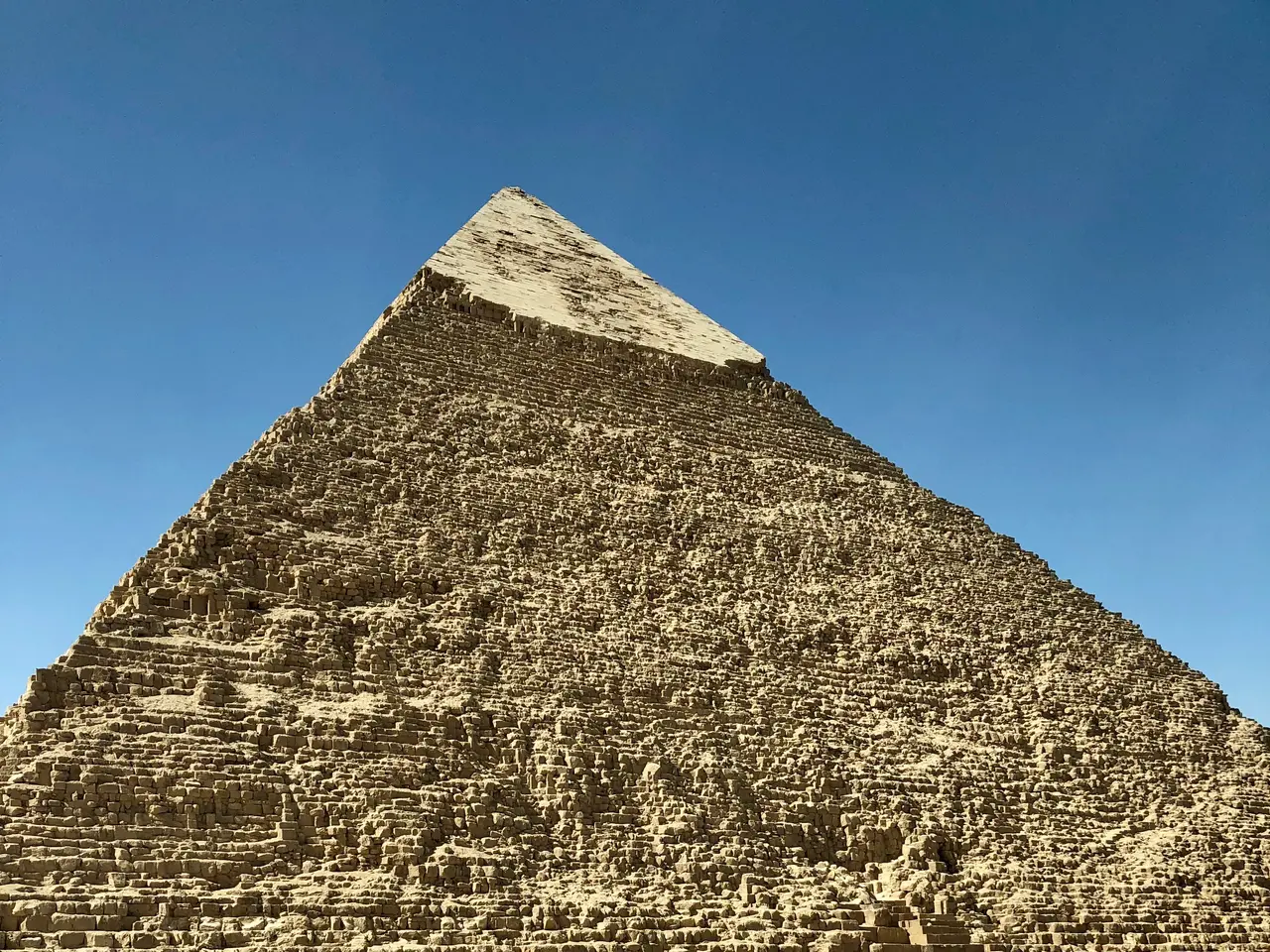 The image shows the great pyramid of Giza, located in Cairo, Egypt. It is surrounded by sand and a...