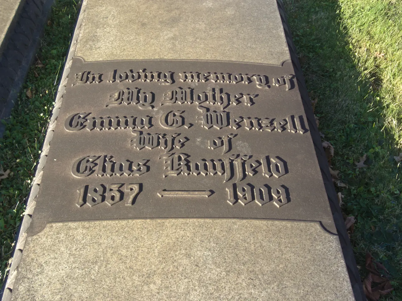 The image shows a gravestone in a cemetery with the words "The Loving Memory of My Mother"...
