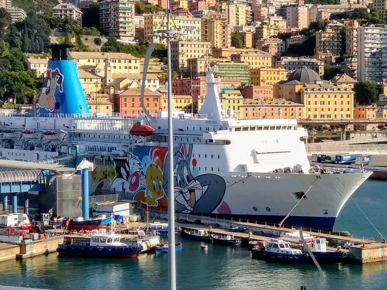 The image shows a large cruise ship docked in the water near a city, with a bridge on the left side...