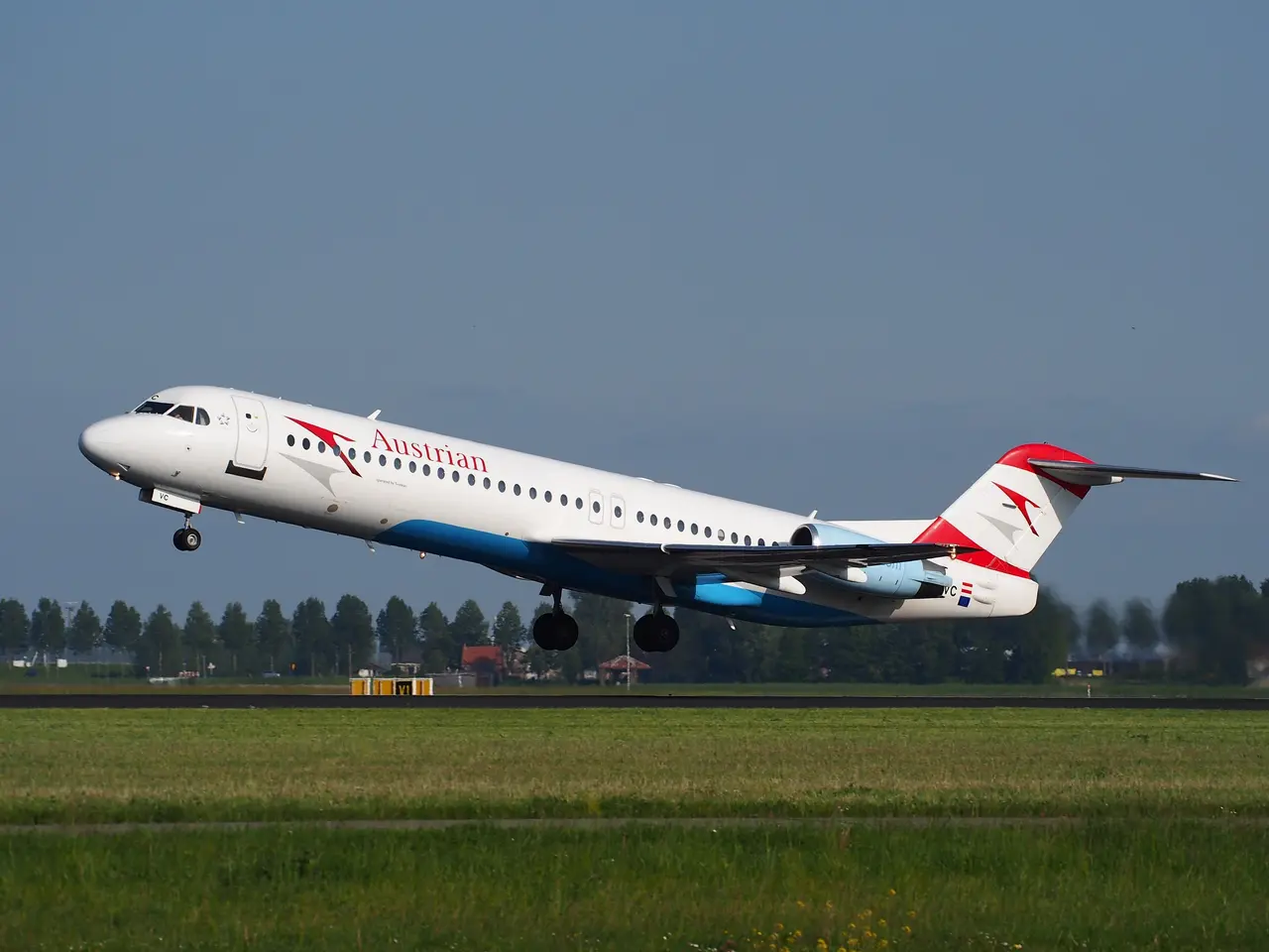 The image shows an Austrian Airlines Embraer ERJ-190 taking off from Frankfurt Airport, with lush...