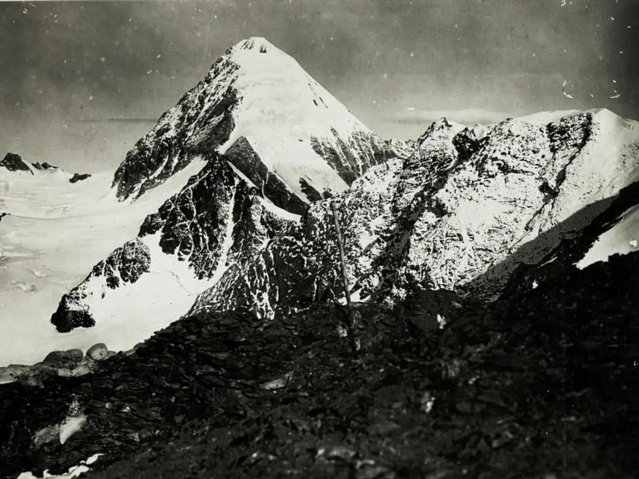 The image shows a black and white photo of a snow-covered mountain, with the sky in the background....