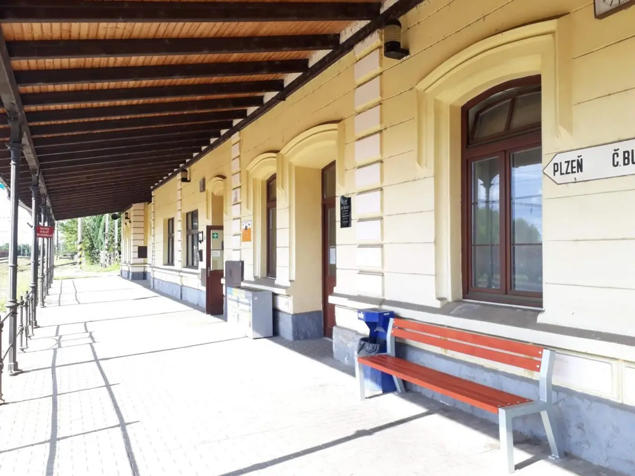 The image shows a train station with a bench sitting on the side of it. The building has windows...