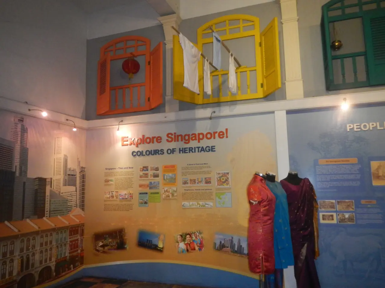 The image shows a room filled with mannequins wearing dresses, a wall with text and pictures, a...