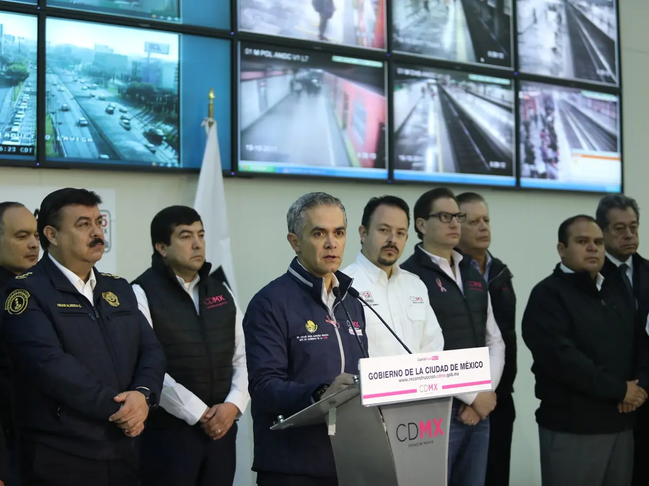 The image shows a group of men standing next to each other in front of a podium with a microphone...