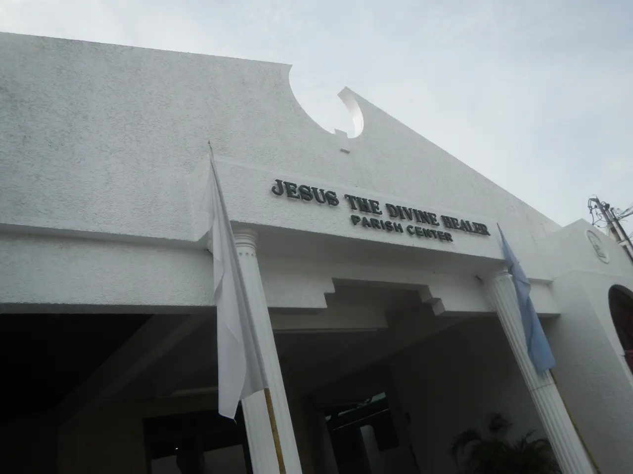 The image shows Jesus the Divine Healer Parish Center, a building with text on the wall, pillars,...