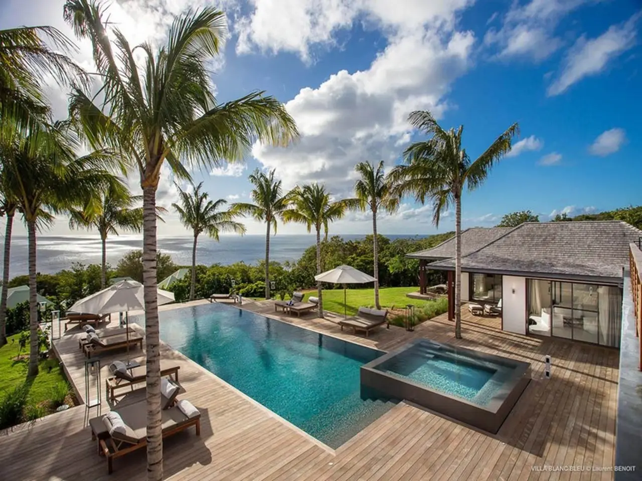 The image shows a luxurious villa with a swimming pool surrounded by lush green grass, trees, and...