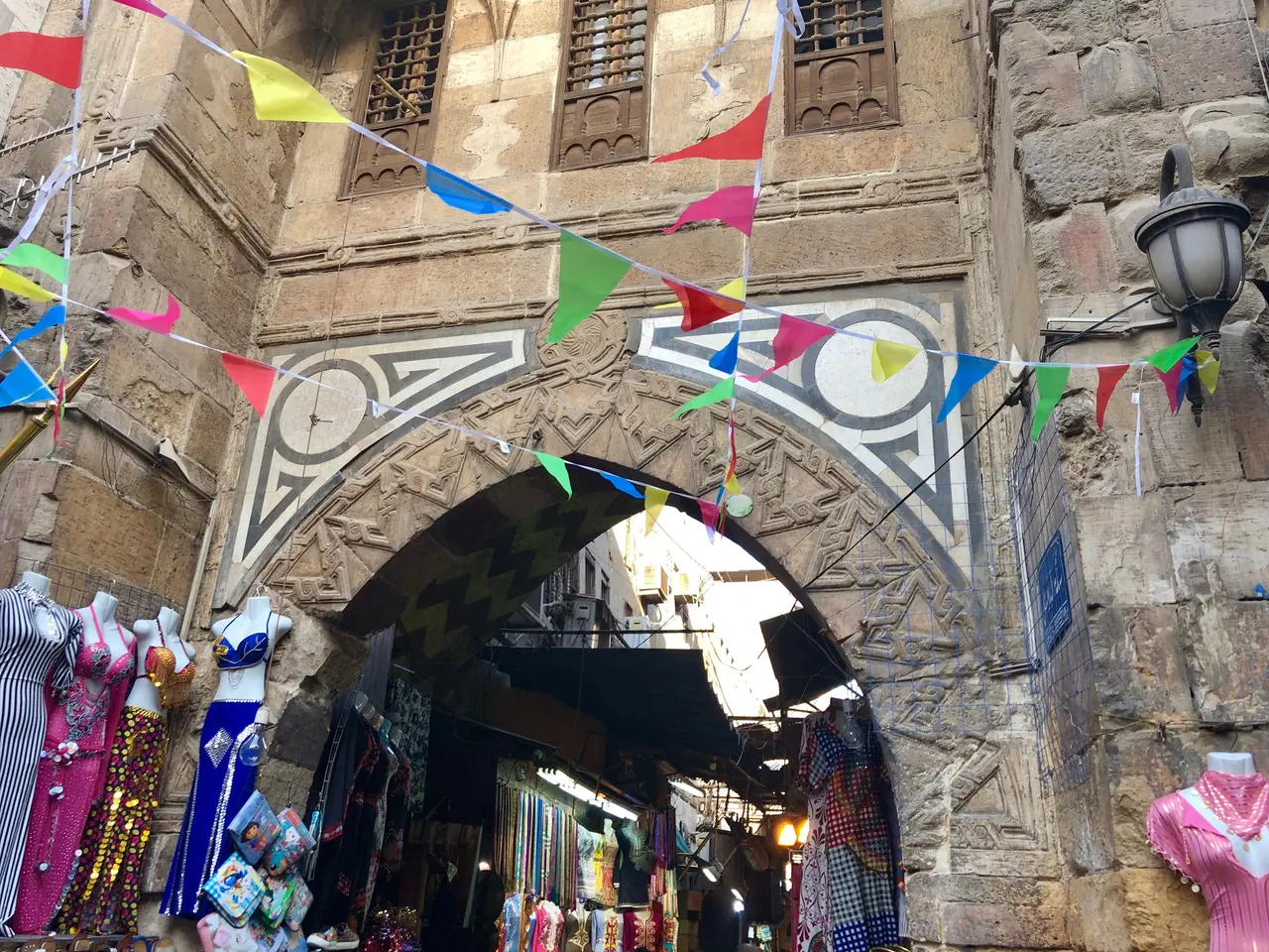 The image shows a narrow street with mannequins in the middle of it, surrounded by buildings with...