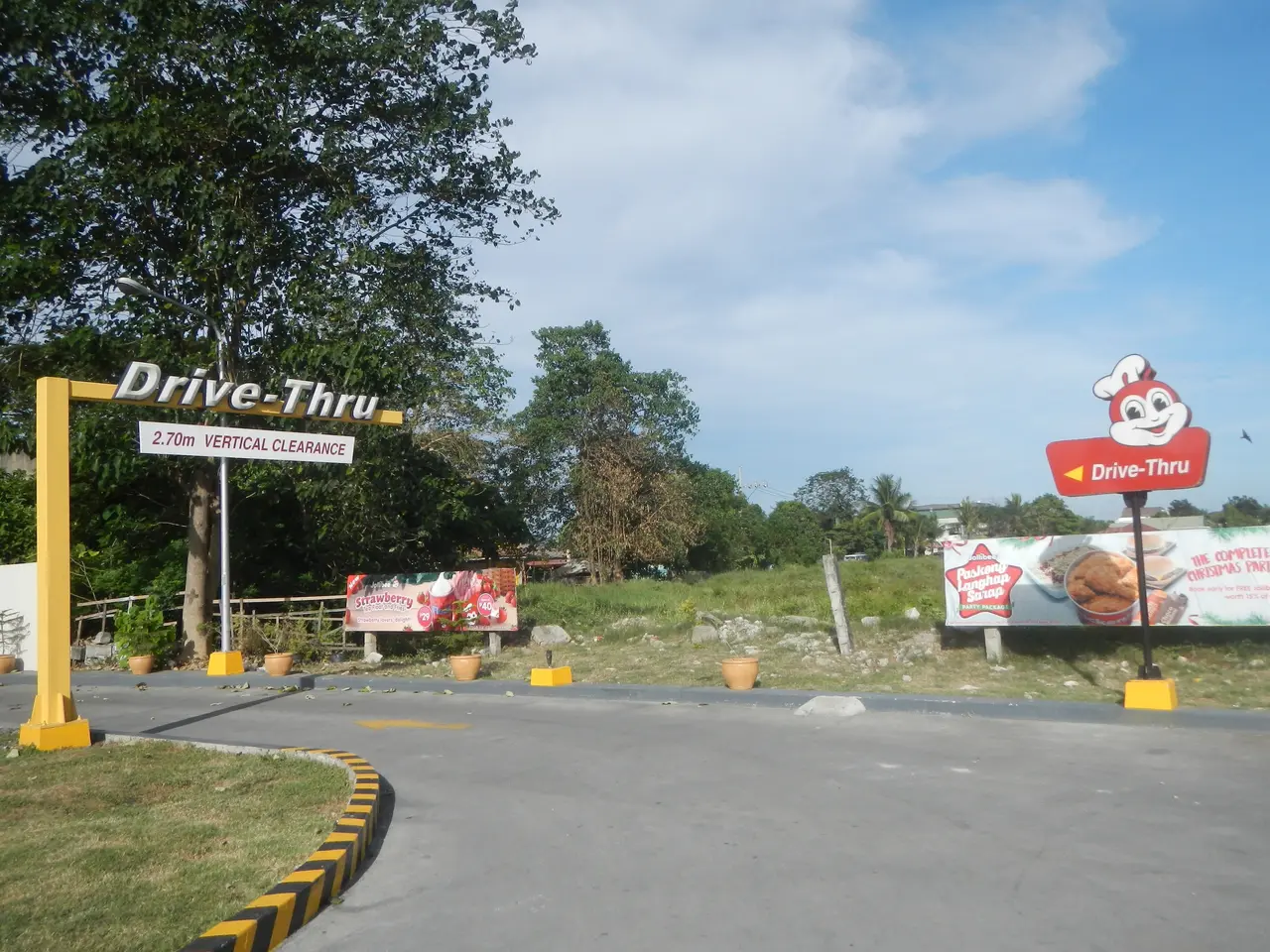 The image shows the entrance to a drive-thru restaurant in the Philippines, with a road, grass,...