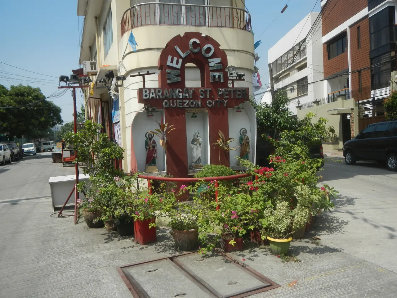 The image shows a building with a sign that reads "Welcome to Barangay St. Peter Quezon City"...