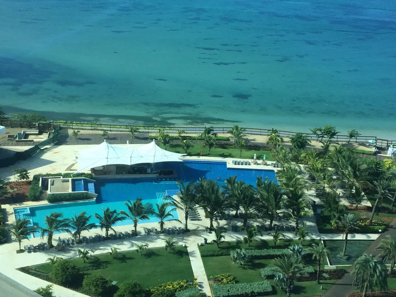 The image shows an aerial view of a resort with a large swimming pool surrounded by lush green...