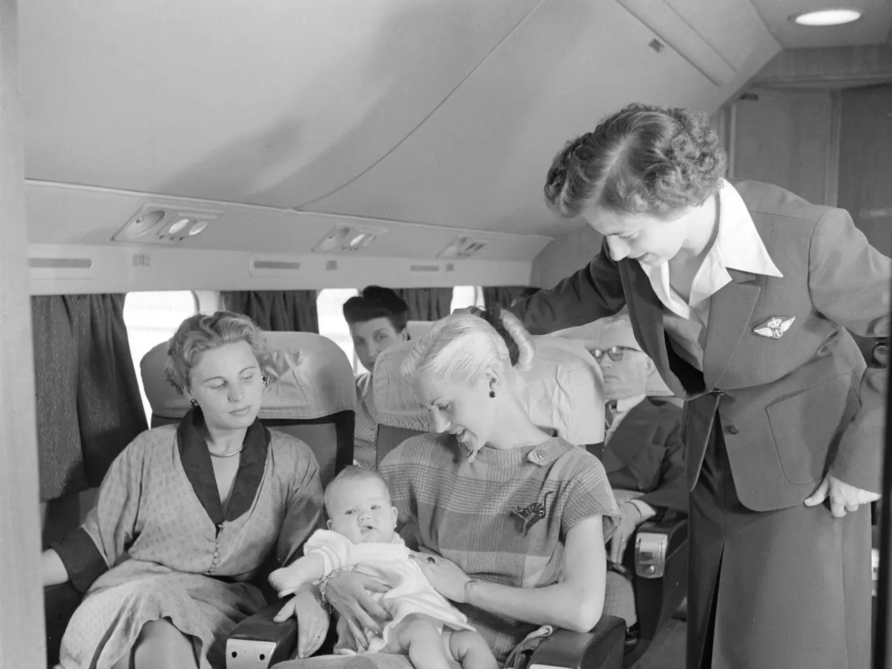 The image shows a black and white photo of a flight attendant standing on the right side of the...