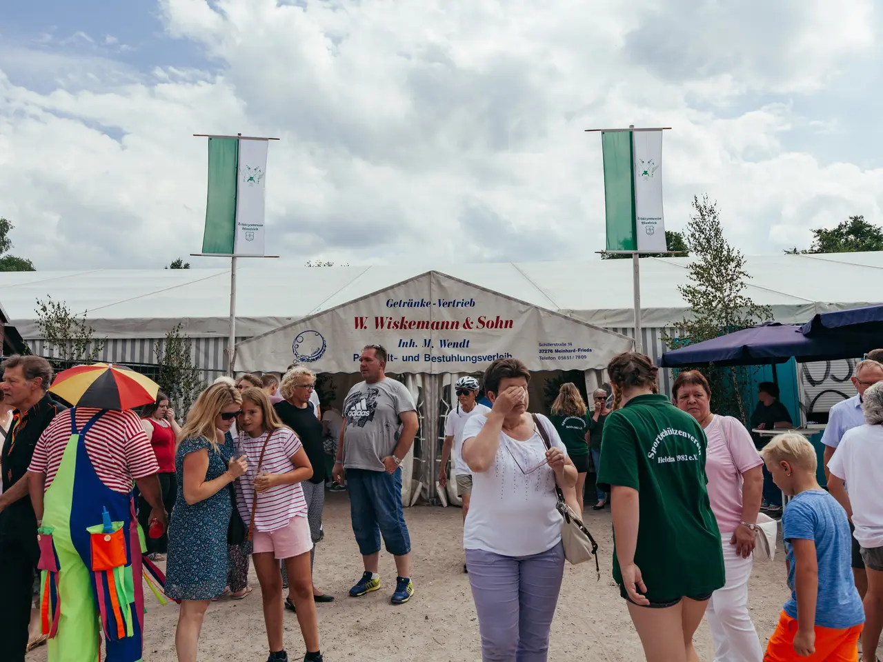 The image shows a group of people standing in front of a tent at a festival. Some of them are...
