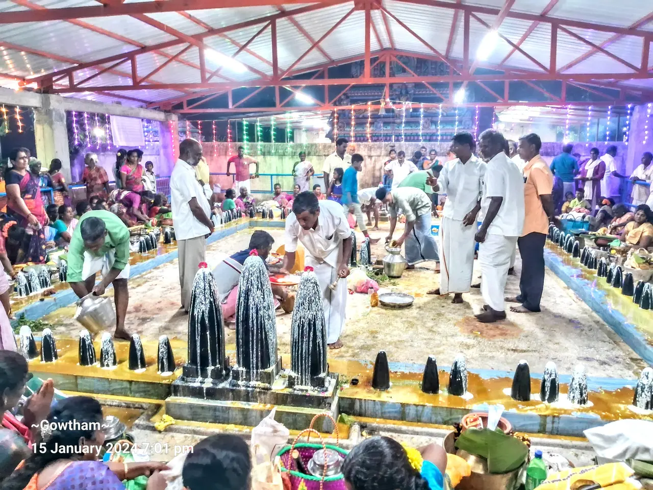 The image shows a group of people standing around a large group of water fountains in a temple....