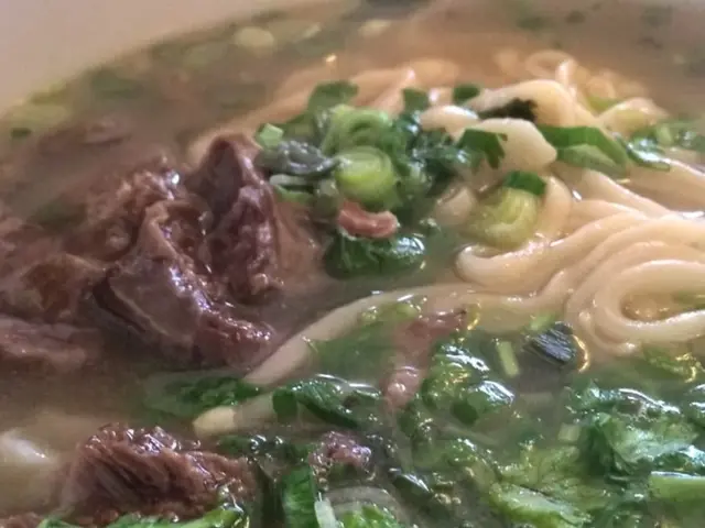 Here we can see a food item with soup,noodles and some other items in a bowl.