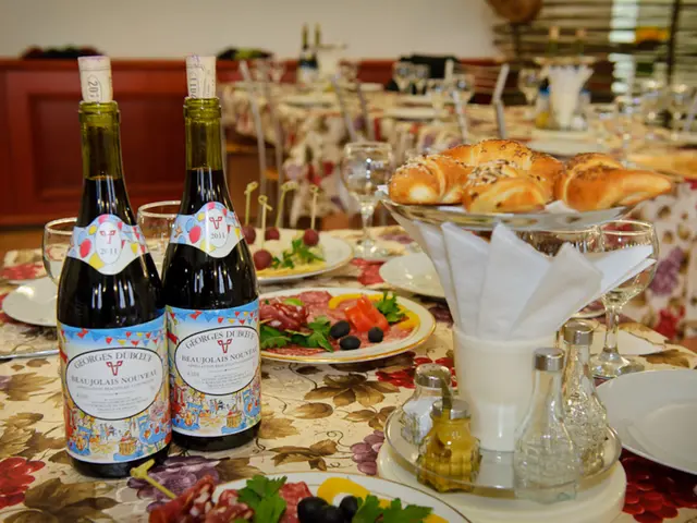 There are two wine bottles,glasses and some eatables in plates arranged on a table.