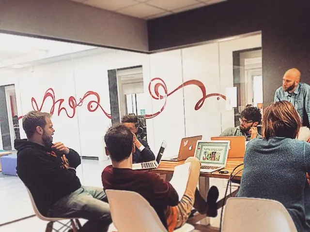 In this picture i could see many men sitting around the table and working on the laptop. In the...