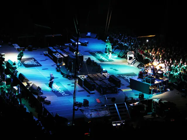 This image consists of few people performing on the dais. On the days, we can see many boxes and...