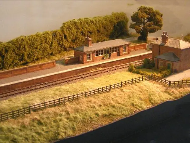 This image is an art. In the middle, there are houses, platform, railway track, trees, fence,...