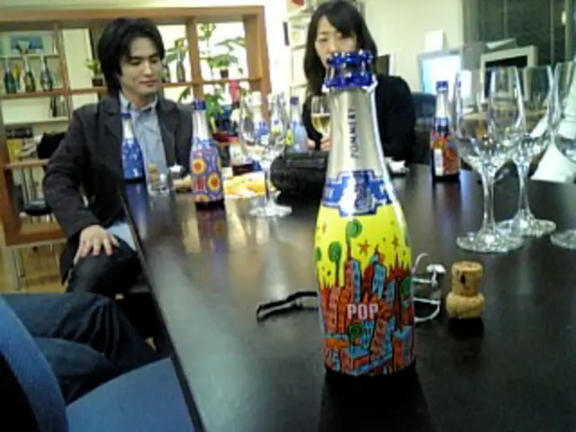 This image consists of three persons and we can see a table on which there are bottles and wine...