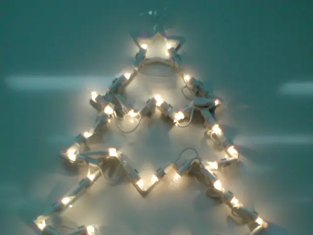 In this picture, I can see structure of a Christmas tree with lighting on the wall.