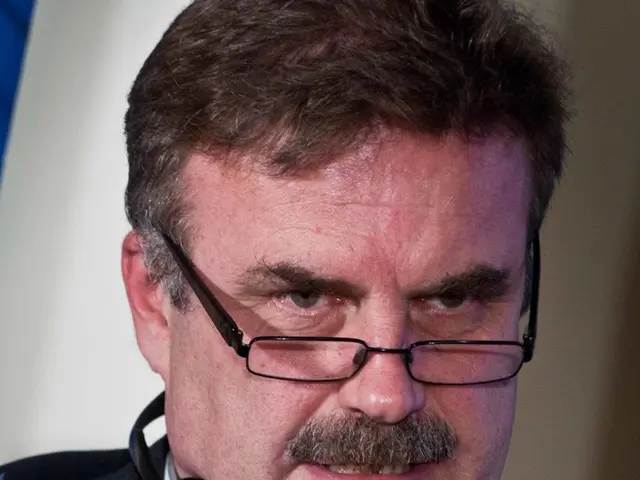 As we can see in the image there is a man wearing spectacles, black color coat and holding a mic...