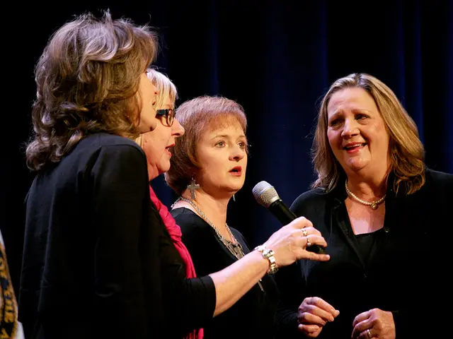 The women wearing pink is standing and holding a mic in her hand and there are three other people's...