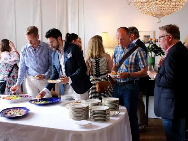 In this picture there are many people eating food and there is a white table on top of which food...