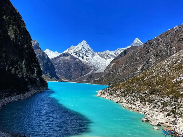 The image shows a group of people standing on top of a mountain next to a body of water, surrounded...