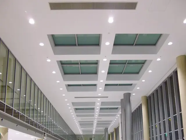 The image shows a long hallway in an airport with people walking through it. On the right side of...