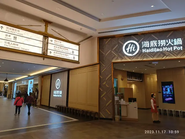 The image shows the lobby of a hotel with people walking through it. There are boards with text on...