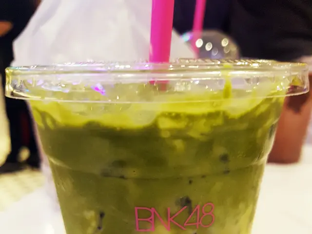 The image shows a cup of green tea with a pink straw sitting on top of a white plate on a table. In...