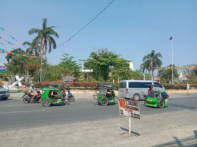 The image shows a group of people riding motorcycles down a street lined with trees, plants,...