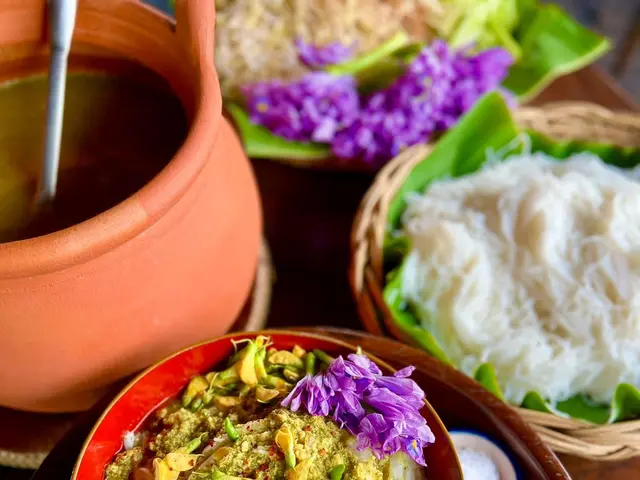 The image shows a wooden table topped with bowls filled with food and a pot of soup, as well as a...