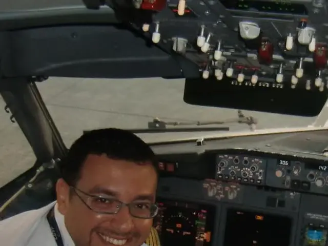 The image shows two men sitting in the cockpit of an airplane, both wearing white uniforms and...