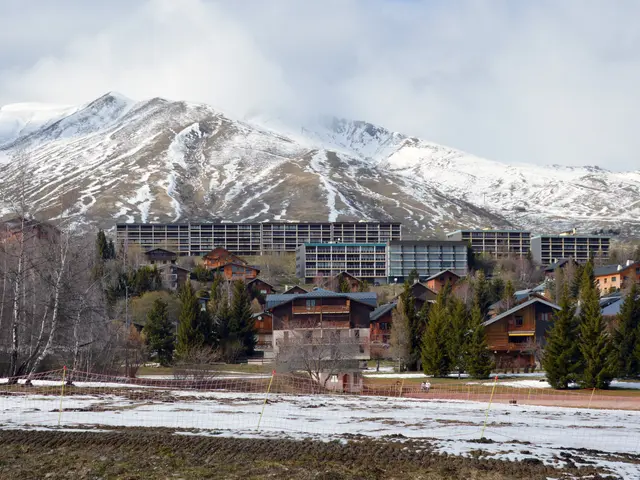 The image shows a picturesque view of a ski resort with snow-covered mountains in the background....