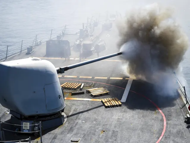 The image shows a navy ship firing a gun on the deck of the USS George H W Bush CVN-68, with smoke...