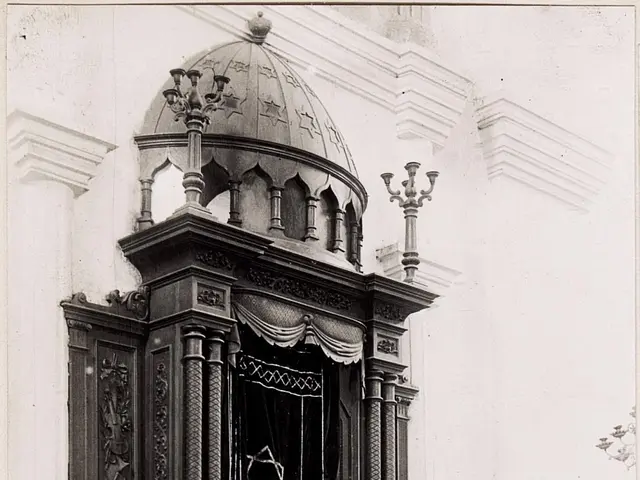 The image shows an old black and white photo of a building with stairs, railings, pillars, a door,...