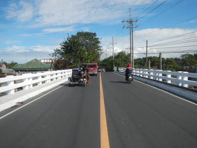 The image shows a group of people riding motorcycles across a bridge with railings on either side....