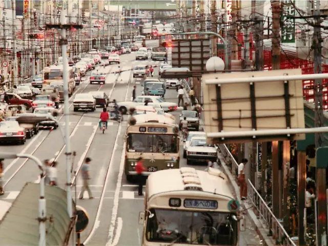 The image shows a city street filled with lots of traffic, including buses, cars, and people. There...