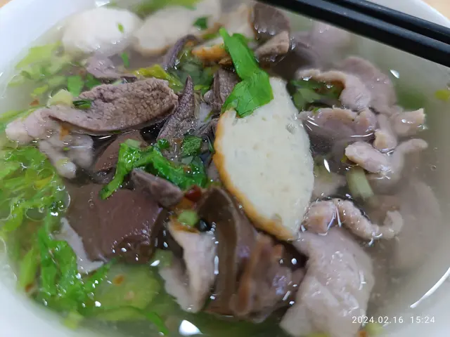 The image shows a bowl of soup with meat and vegetables in it, placed on a table with a pair of...