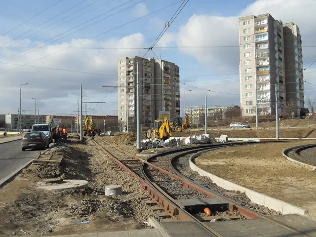 The image shows a construction site with a train track running through it, surrounded by buildings,...